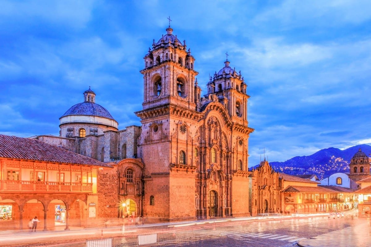 Cusco-Peru-4-Landed-Travel-Private-Travel Historic light orange church with two domed towers, lit up at dusk in Cusco-Peru