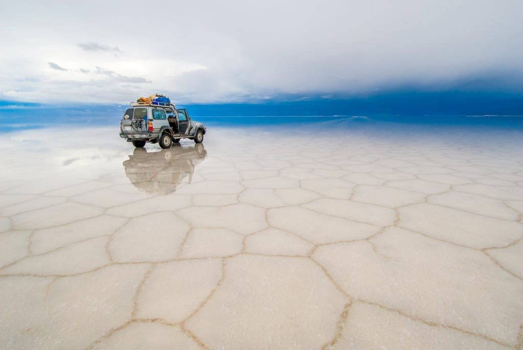 Uyuni-Bolivia-Landed-Travel-Private-Travel Offroad vehicle parked on fragmented glass-smooth salt flats of Uyuni, Bolivia, seemingly endless and backed by a clear blue sky