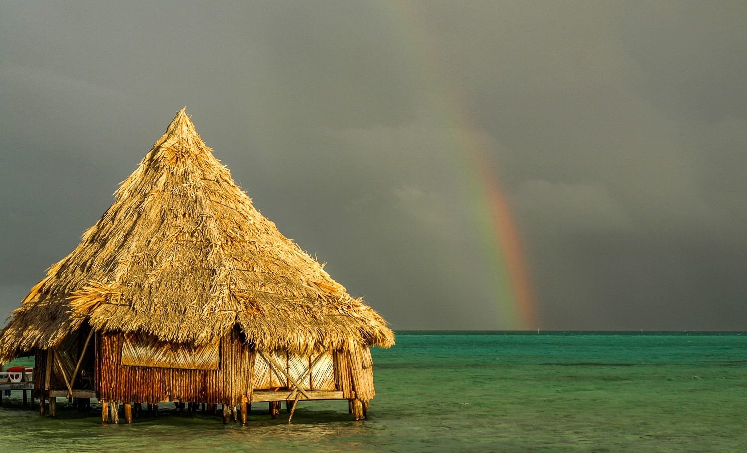 Overwater-Bungalow-Caye-Belize-Rainbow A rainbow over the straw roof of and ocean surrounding an overwater bungalow in Belize