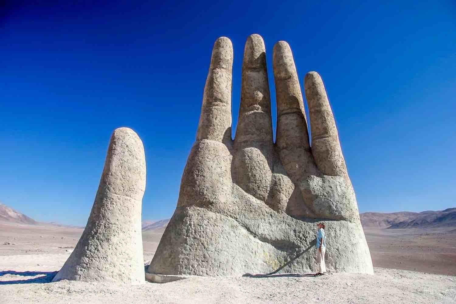 Desert Palm Man on vacation in Chile, admiring Desert Palm - Mano del Desierto, a giant white sculpture of a human hand, buried to the middle of the palm with fingers outstretched Antofagasta, Chile