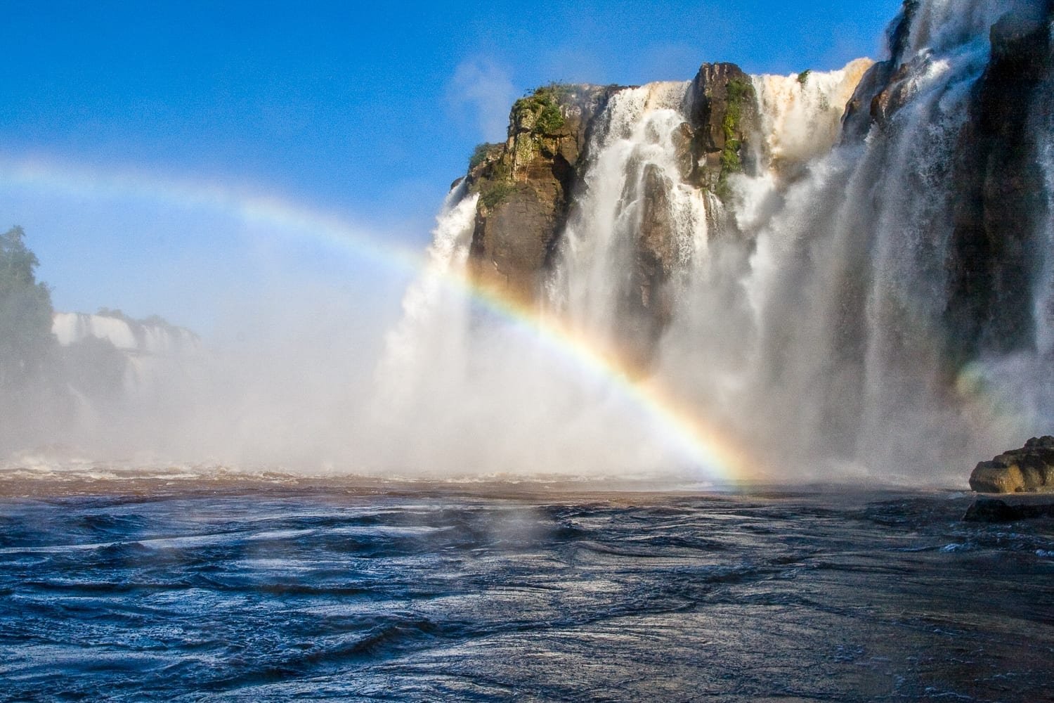 Custom-Travel-Iguazu-Falls-Argentina-Rainbow-River Rainbow over the river at Iguazu Falls, large white waterfall in background