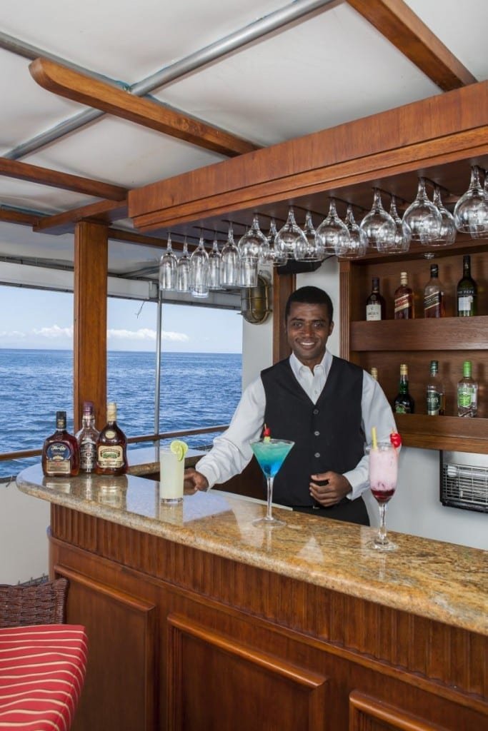 Grace-Bar Bartender onboard M/V Grace, Galapagos Yacht Charter, wearing black vest behind an elegant blue martini