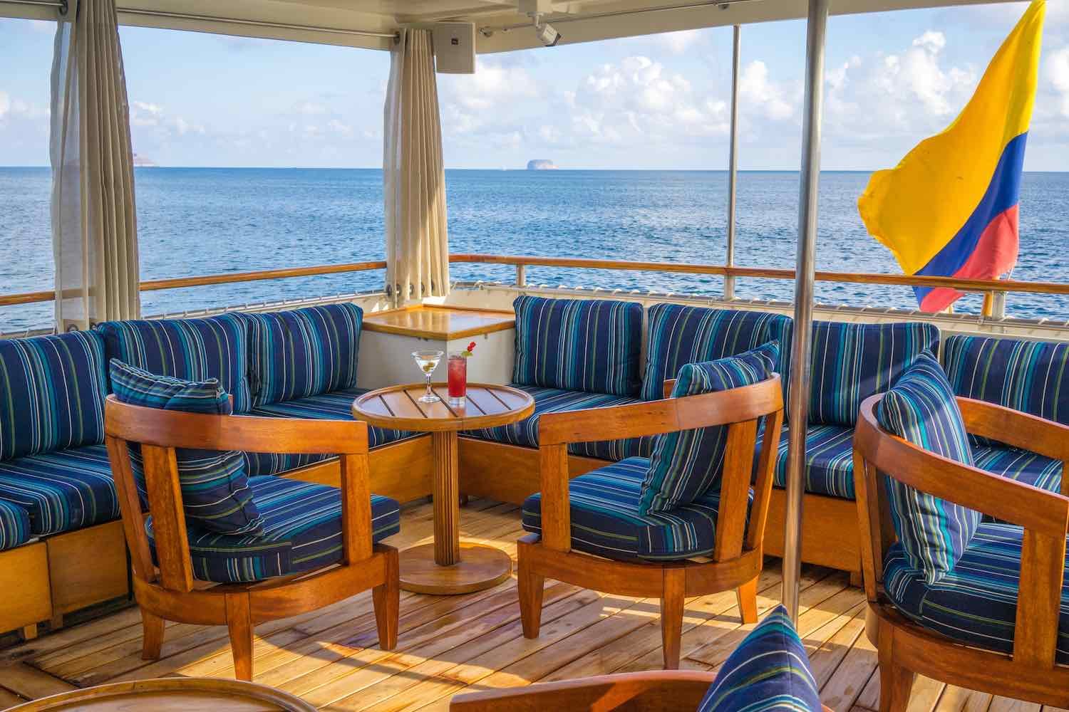 Grace-Outside-Saloon-3 Blue striped L-shaped seating area overlooking the Galapagos onboard M/Y Grace, a Galapagos Yacht Charter