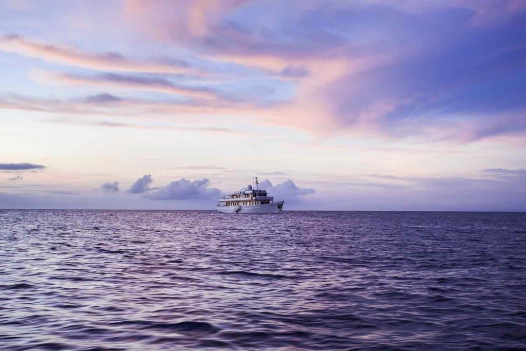 Grace-Sunset-2 Large, white, Galapagos Yacht Charter M/Y Grace, cruising the waters off the Galapagos Islands at sunset, purple sky in backdrop