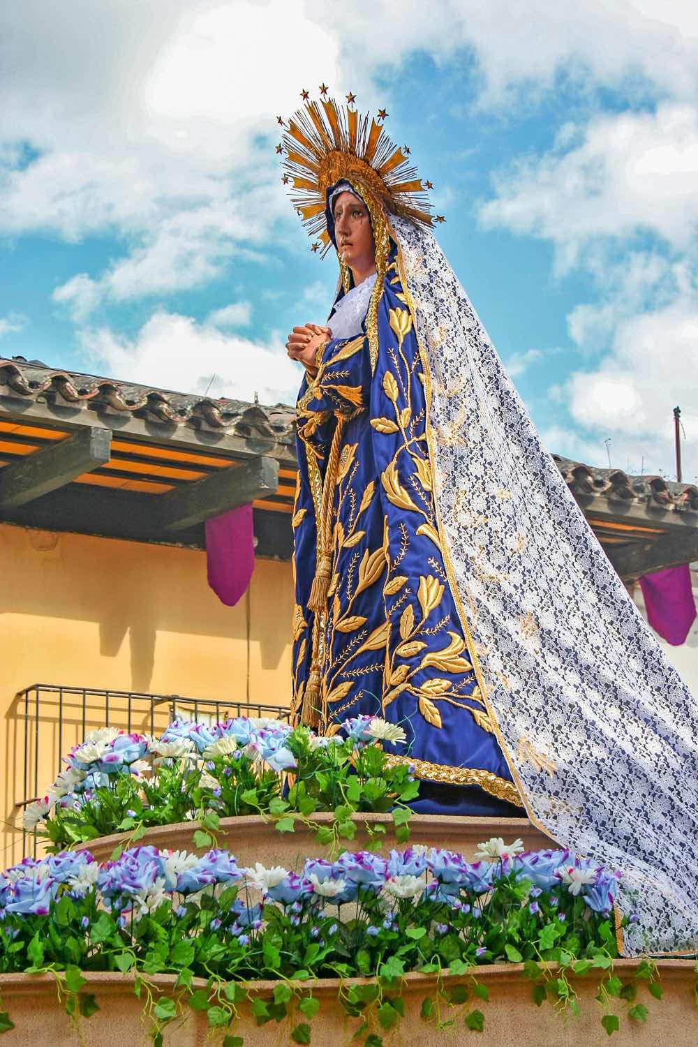 Guatemala-Private-Custom-Travel-Design-Antigua-Semana-Santa Large effigy of Santa Semana, wearing a purple robe with gold pattern, crown and long flowing purple and white head dress, On display at Festival in Guatemala