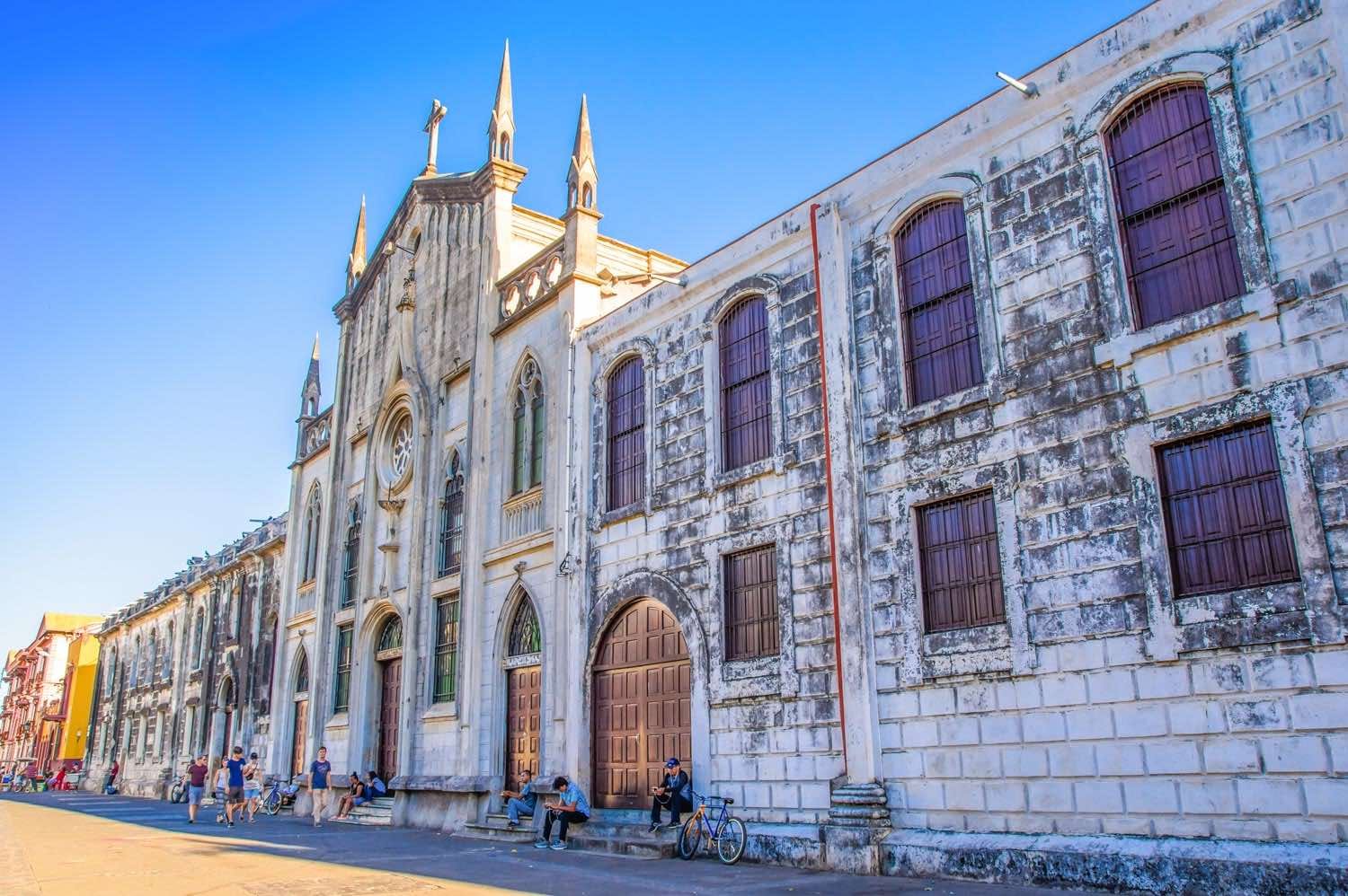 Landed-Travel-Private-Travel-Church-Leon-Nicaragua Photo taken down a street showing a weathered White stone church and row of historic buildings in Leon, Nicaragua,