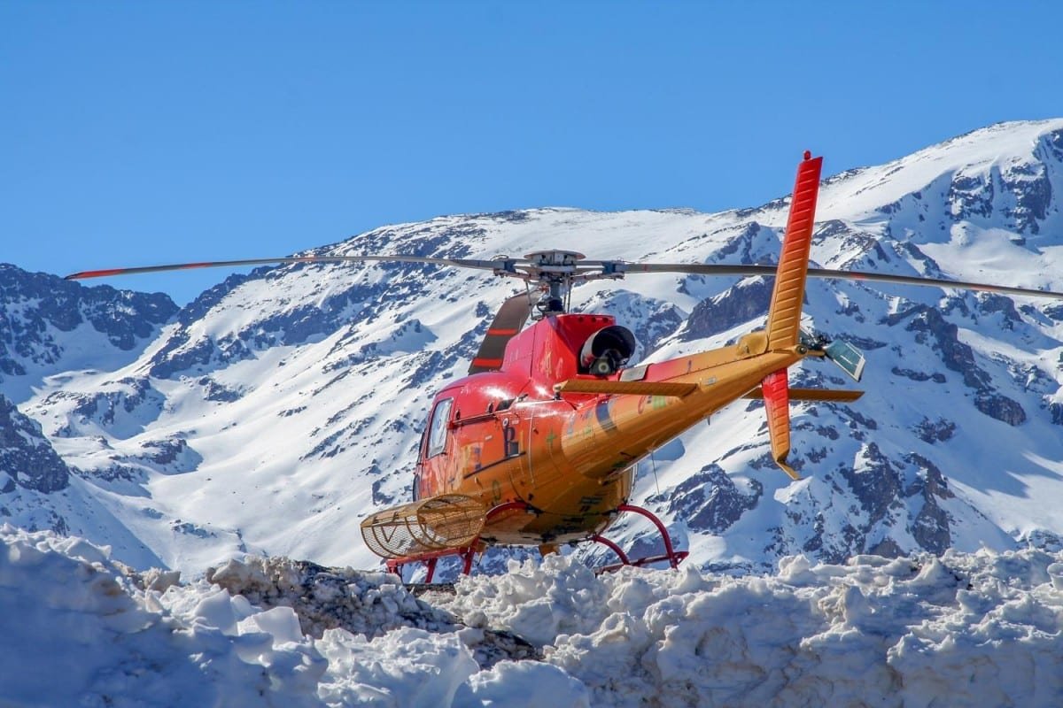 Landed-Travel-Private-Travel-Heliski-Chile-Red Helicopter flying up a mountain run in the Chilean Andes, preparing to drop a group of leisure travelers off for a heliski adventure