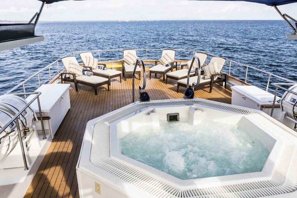 Yacht-Charter-Galapagos-Stella-Maris Large, white octagonal hot tub on deck of Stella Maris Galapagos Yacht, overlooking the ocean around the Galapagos Islands with white lounge chairs in background