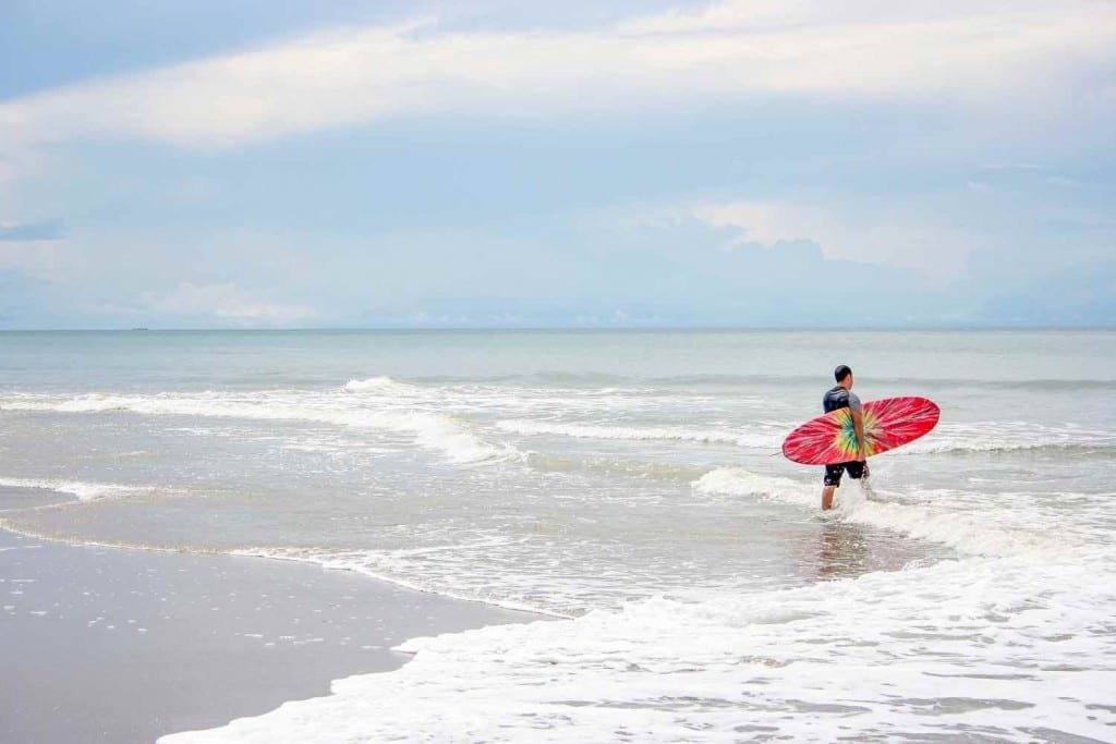 Panama-Custom-Travel-Design-Pacific-Beach-Surf-Sunny Surfer holding red surfboard, preparing to surf the waves off of the Pacific Coast of Panama