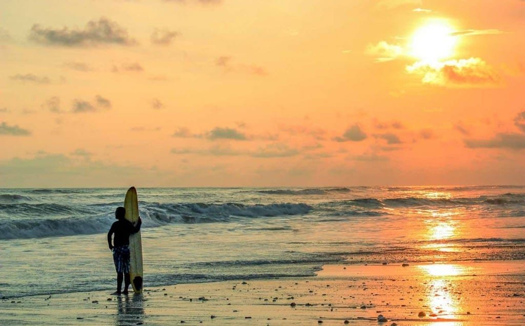 Panama-Custom-Travel-Design-Pacific-Beach-Surfer-4 A surfer on leisure travel holding his surfboard after a day of surfing, watching the orange sunset over the beach in Panama
