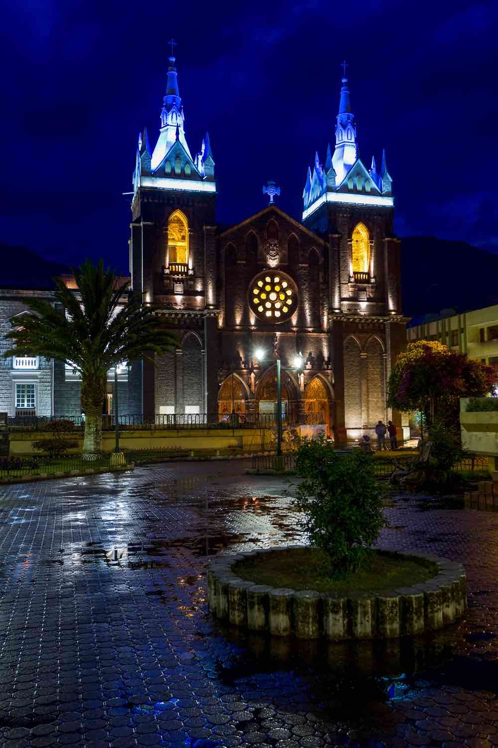 Private-Travel-Custom-Travel-Ecuador-Banos-Church-Night Twin bell towers of Our Lady of the Hold Water Church in Banos, Ecuador, illuminted at night in front of a large courtyard