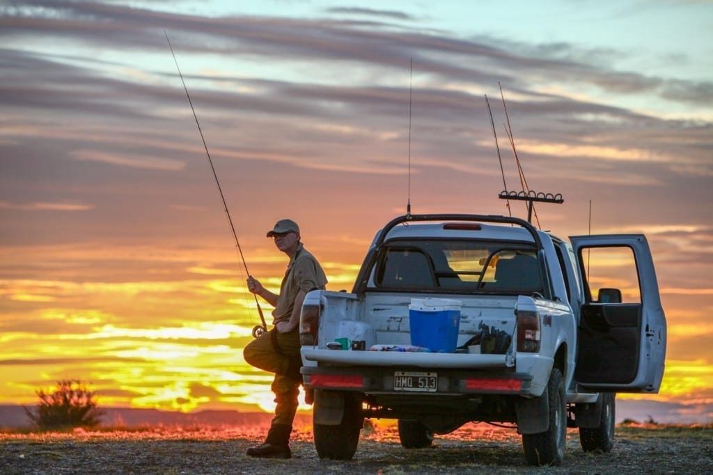 Travel-Fly-Fishing-Rio-Gallegos-Patagonia-Argentina Man with a fishing pole leaning agains a white four-wheel drive vehicle at sunset in Argentine Patagonia