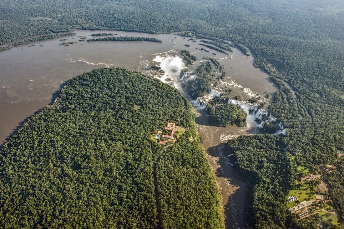 Private-Custom-Travel-Design-Brazil-Iguacu-Aerial-Wide Aerial photo taken from helicopter charter tour over Iguacu falls in Brazil showing the massive brown Iguacu river surrounded by dense forest