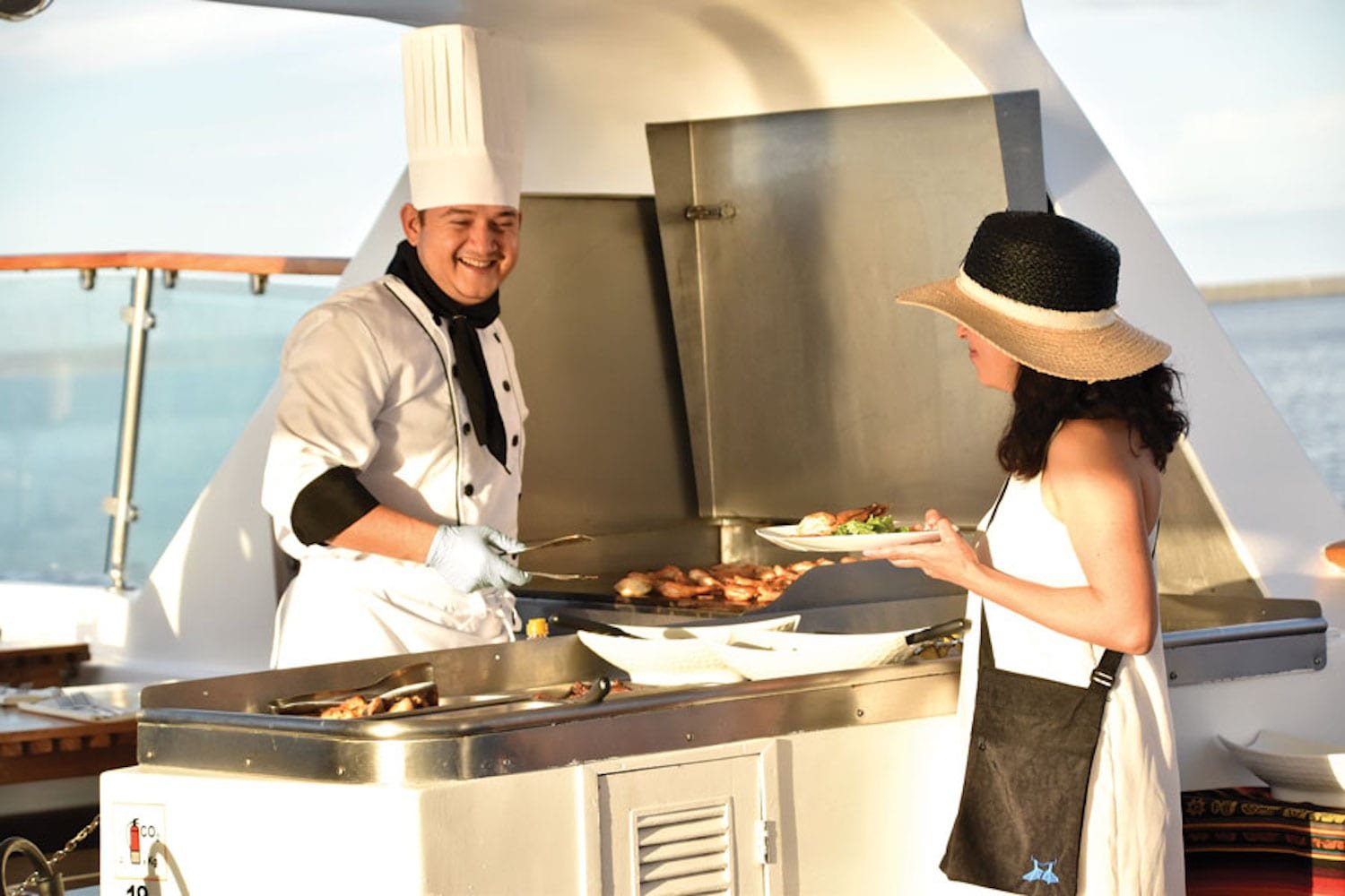 bbqatsundeck Man in chef hat cooking al fresco BBQ for Woman on Large Galapagos Yacht Charter Cruise Coral II