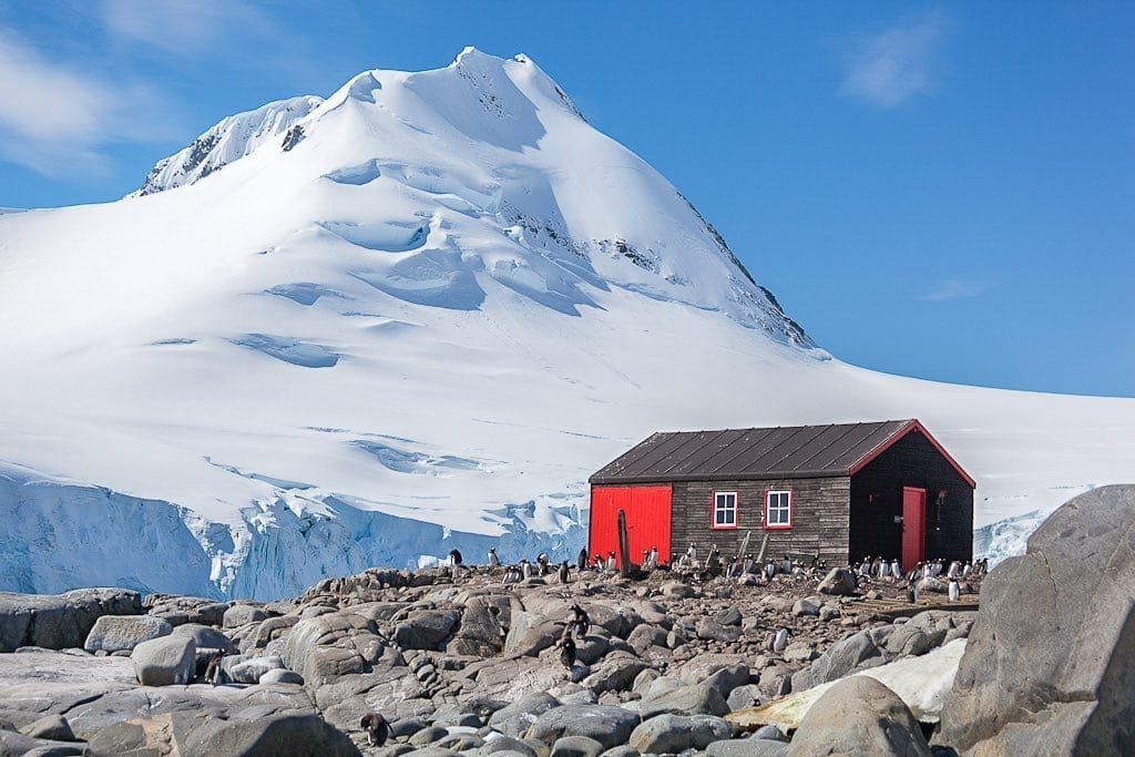 Antarctica-Private-Custom-Travel-Design-Cruise-Antarctica21-5 Small red house backed by large snowy mountain in Antarctica, photographed during a flight to Antartcia single day tour