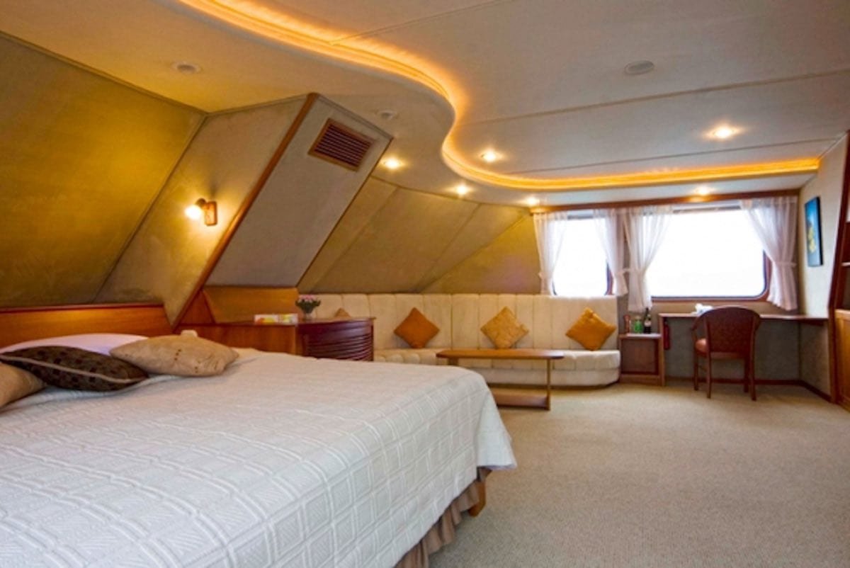 Integrity-Yacht-Charter-Galapagos-2 Executive stateroom onboard Integrity, a fine option amoung Galapagos Yacht Charters with large white king bed and couch near ocean view window