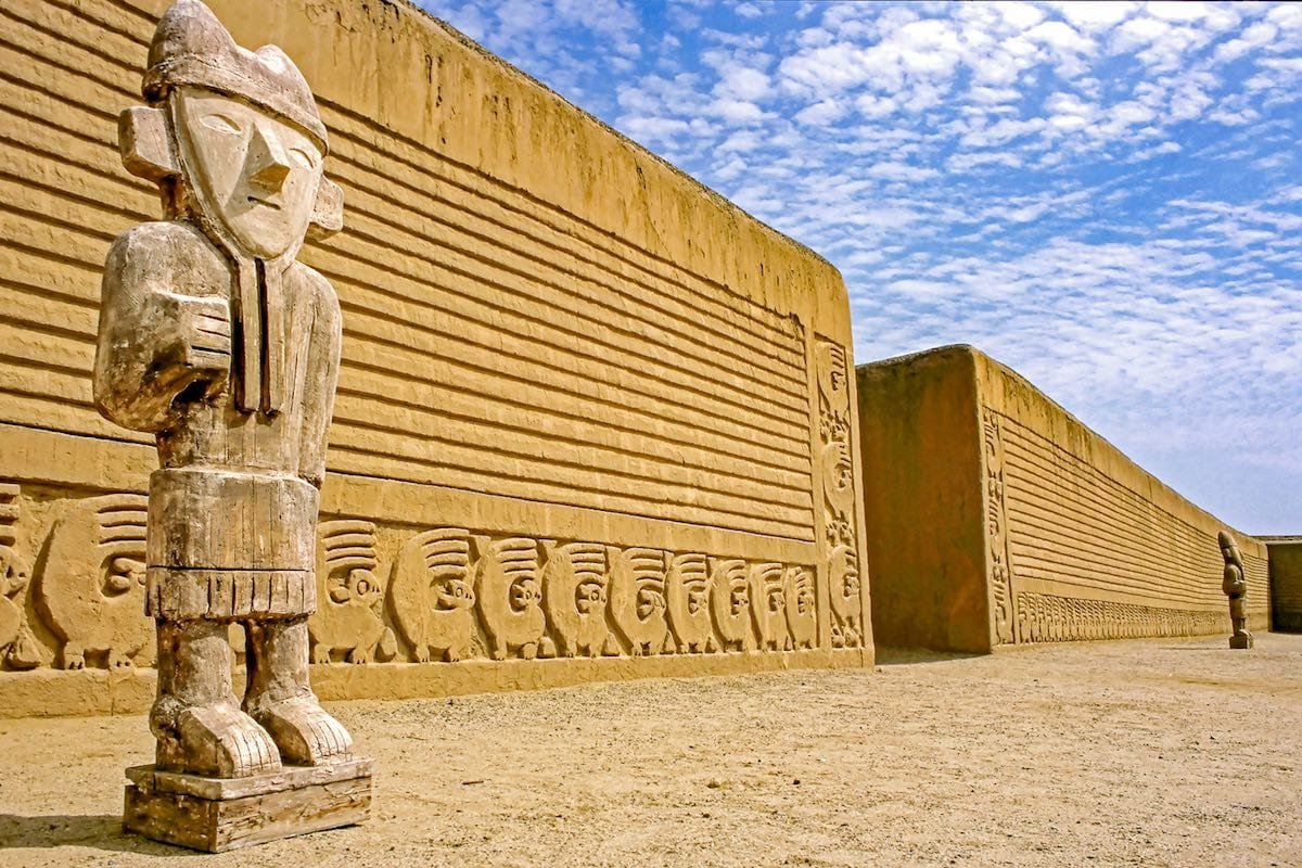 Private-Custom-Travel-Peru-Trujillo-Guards-Chan-Chan An ornate wall with lines and figures carved into its face, behind a detailed ancient statue in Peru