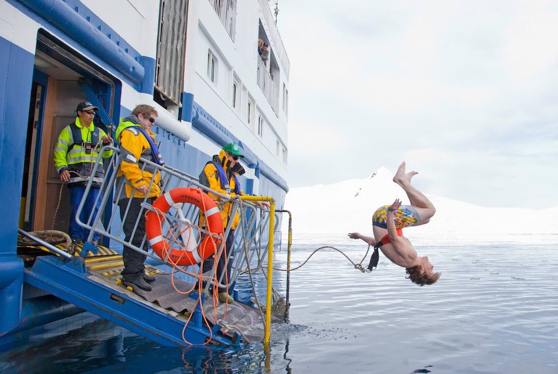 Man-Polar-Plunge-Antarctica A man in a swimsuit with a bungee cord strapped to his waist taking a polar plunge off of a ramp of his Antarctic cruise ship