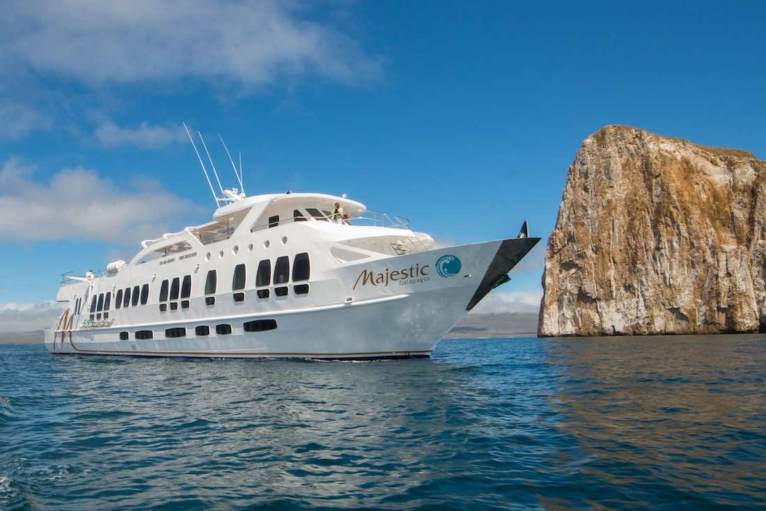 majestic-galapagos-yacht-5 Large white galapagos yacht charter Majestic cruising by a large rock formation in the Galapagos archipelago