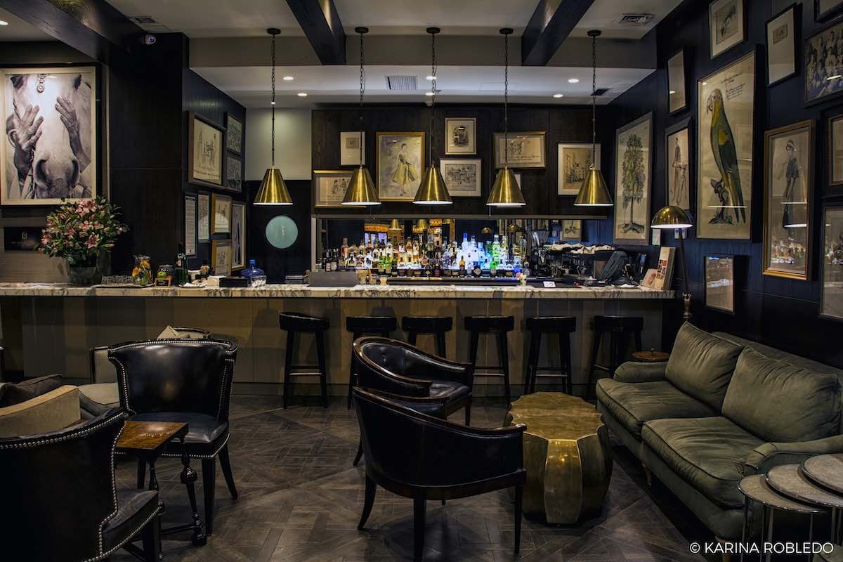 Bar-Merced-Singular-Santiago Singualr Santiago's bar features dark wood furniture low hanging lights. The bar has a variety of drinks on its countertops as well as bar seating.