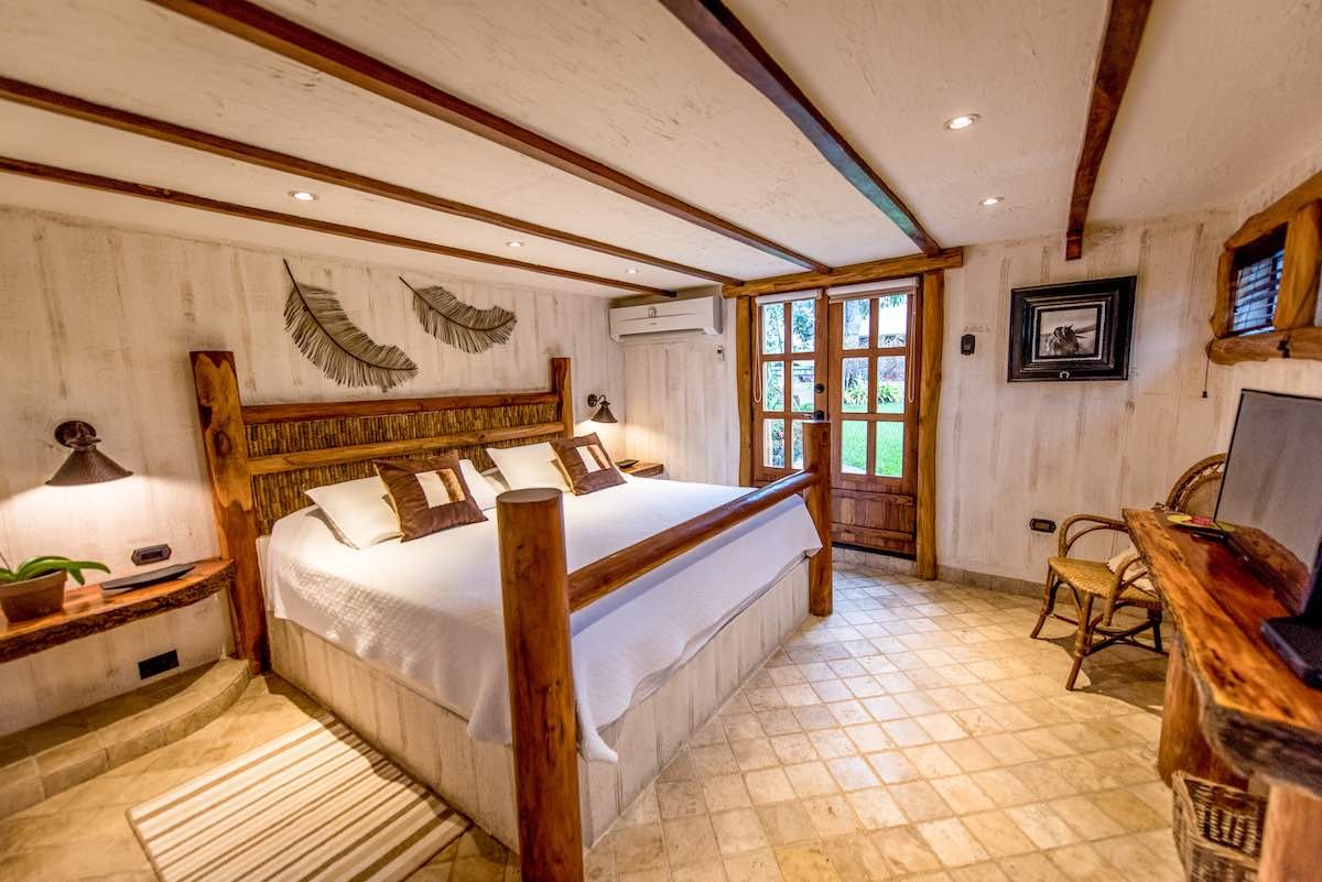Heritage-Bedroom-Hacienda-La-Danesa Hacienda La Danesa's Heritage room has a large while bed, wooden bed frame, and tile floor.