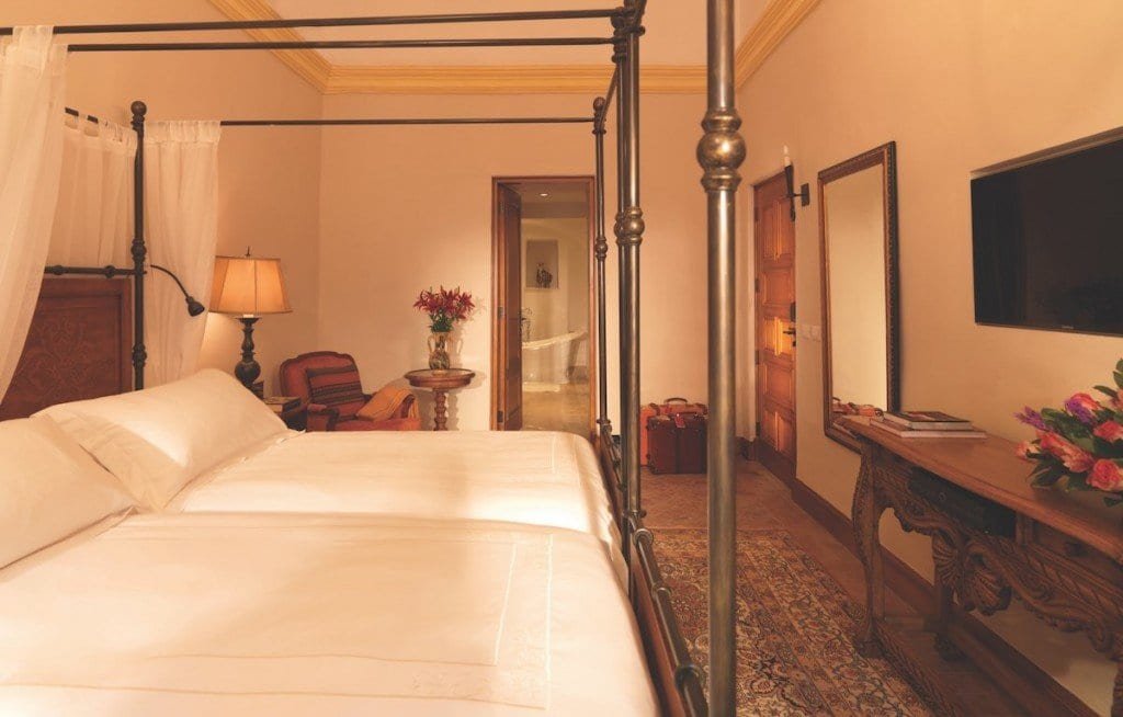 Belmond-Nazarenas-Junior-Suite The junior suites at Belmond Palacio Nazarenas feature two twin post beds, a tv, ornate rug and marble bathroom.