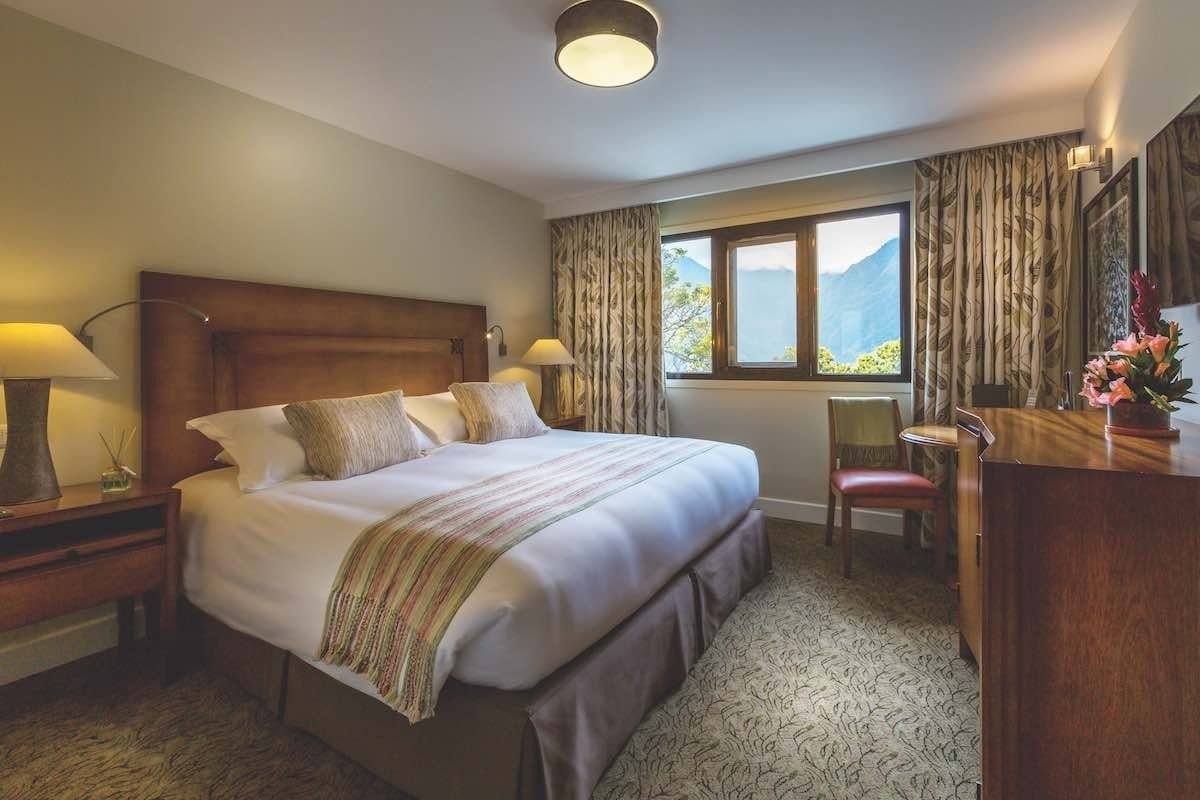 Belmond-Sanctuary-Deluxe-Room This room features a king bed, large window and curtains and carpet.