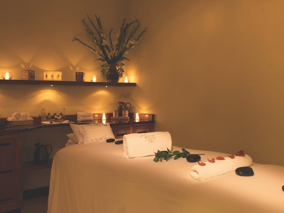 Belmond-Sanctuary-Spa The Spa at the Belmond Sanctuary includes a spa bed with rocks and towels on it.