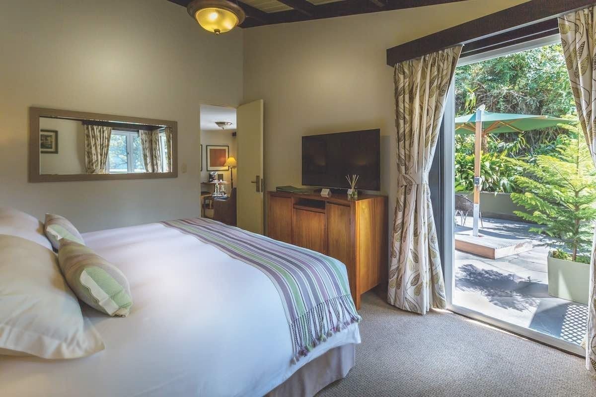 Belmond-Sanctuary-Suite This room features a king bed and patio view of green vegetation.