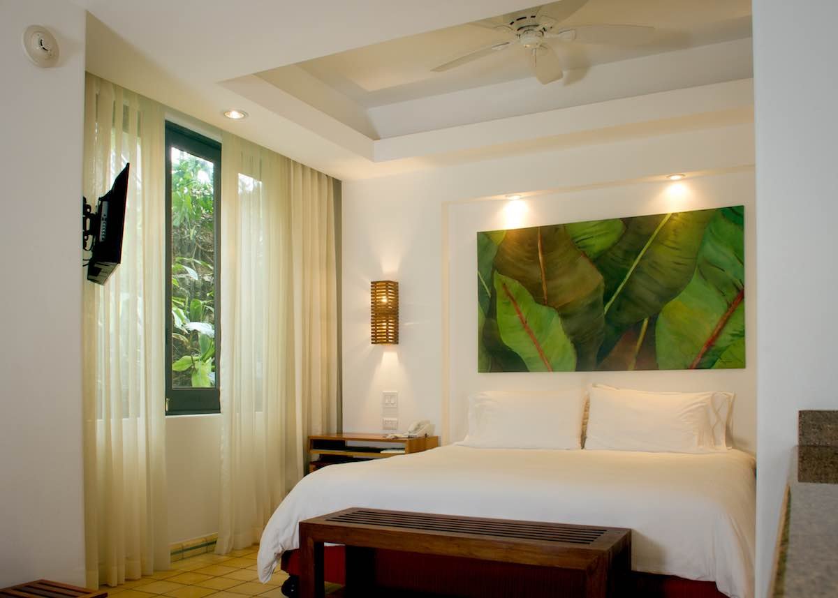 Garden-Room-Arenas-Del-Mar The Garden Room at Arenas del Mar features a king bed, white curtains, wall artwork and bedside tables.