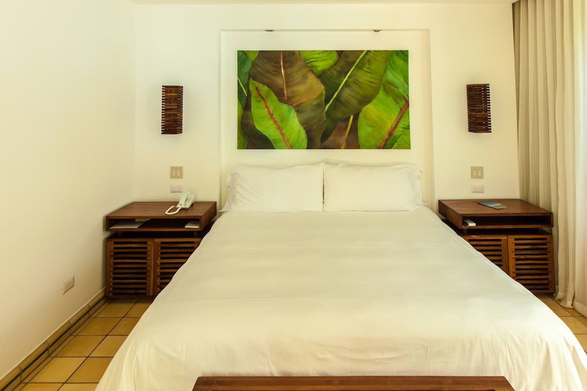 Ocean-Breeze-Suite-Hotel-Arenas-Del-Mar The ocean breeze suite features a king size bed, artwork, bedside tables and wood floors.