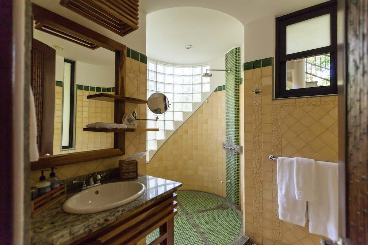 Ocean-Breeze-Superior-Arenas-Del-Mar This bathroom includes a green tiled shower, granite countertops, mirror, sink and towels.