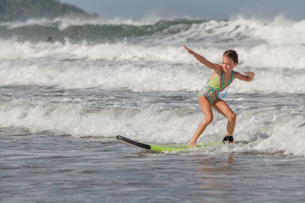 Young girl balancing on a surfboard as she rides a small wave during a beginner surf lesson