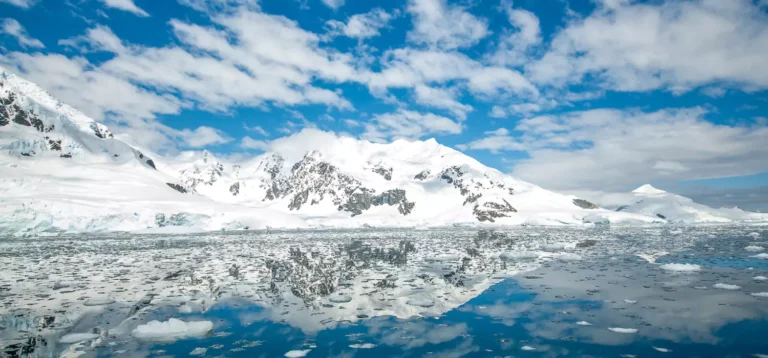 Landscape view of Antarctica - a snowy mountain is reflected in calm waters.
