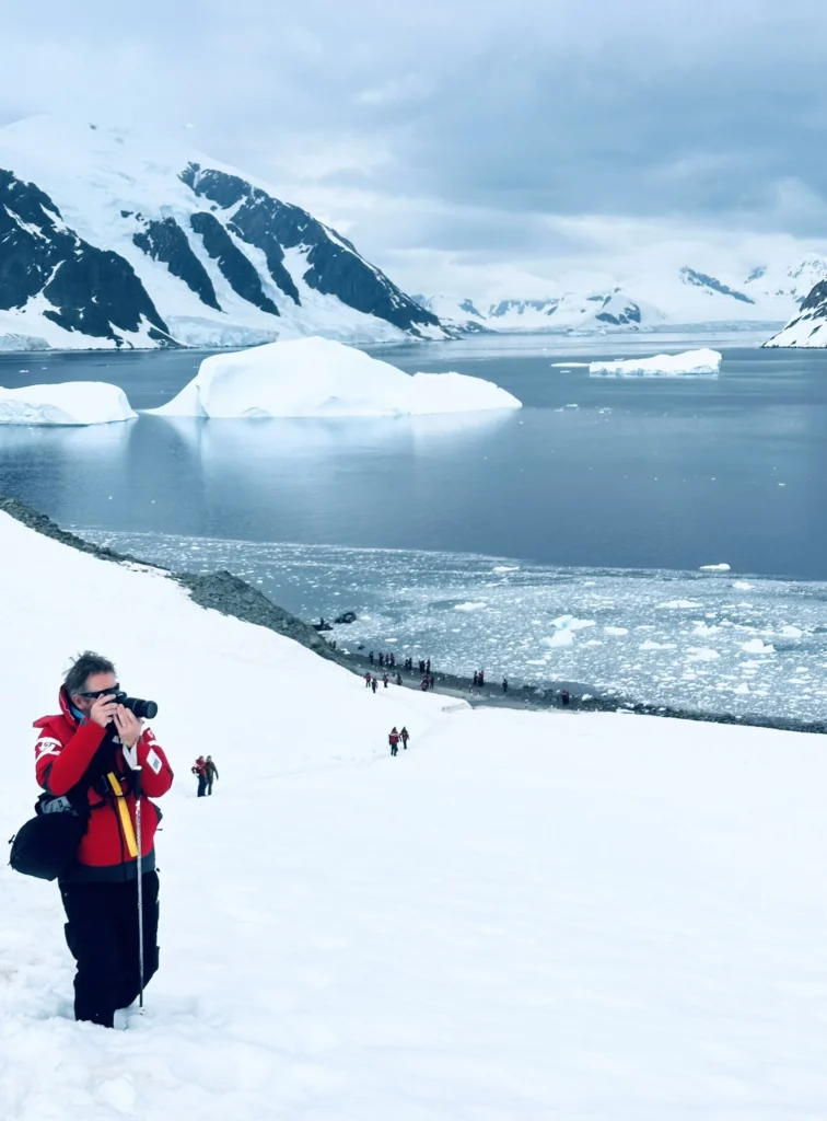 Travel expert talking a picture in the middle of the Antartica snow. The sea and mountains in the back