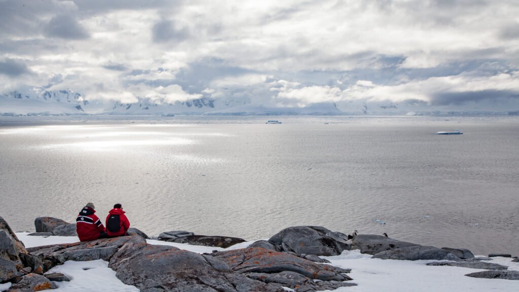 Travelers staring at the sea, sitting on a rock surrounded by snow in Antarctica