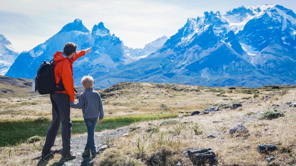 Father and son on a hiking trail pointing toward the snow-capped Cuernos del Paine in Torres del Paine, Chilean Patagonia