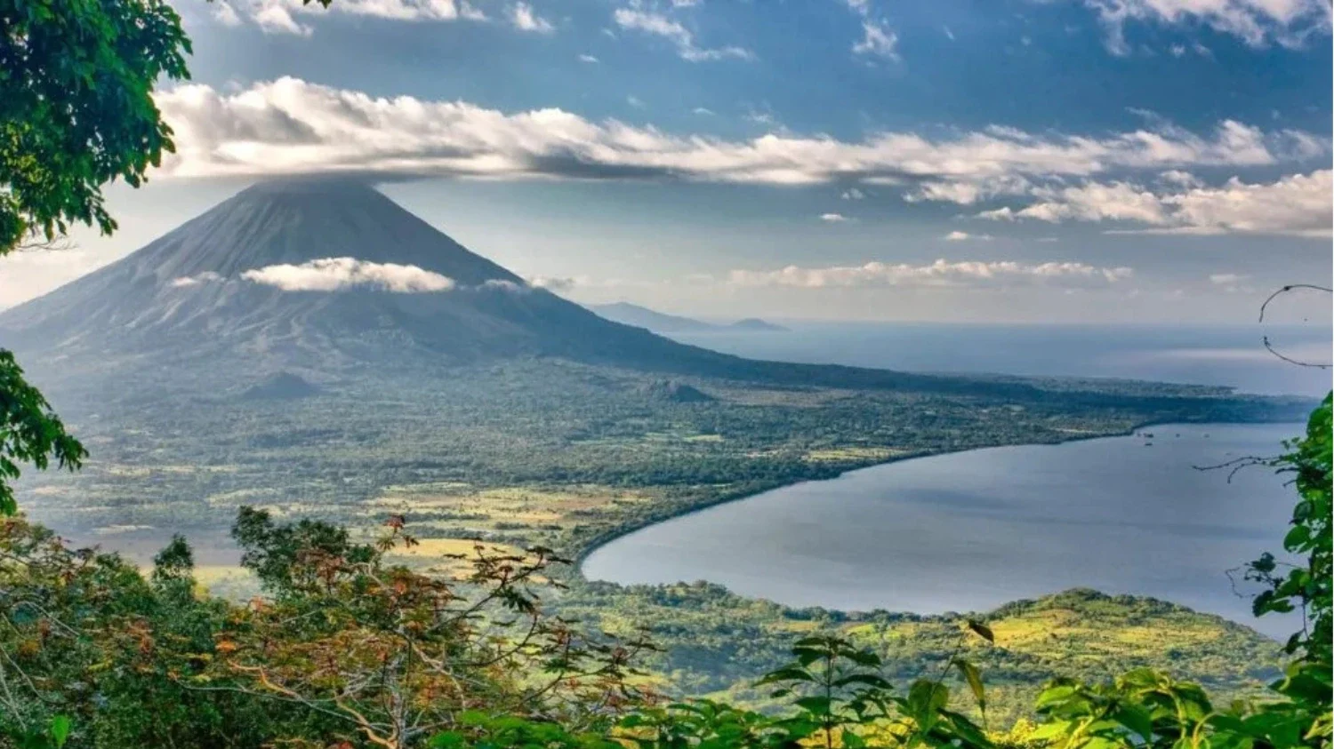 An elevated, wide-angle view of Concepción Volcano on Ometepe Island, Nicaragua, showing its massive volcanic cone sloping down to the forested shoreline of Lake Nicaragua