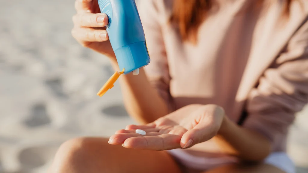 Close-up of a traveler applying sun protective lotion on a sandy beach, highlighting essential sun protection and gear prep for tropical destinations.