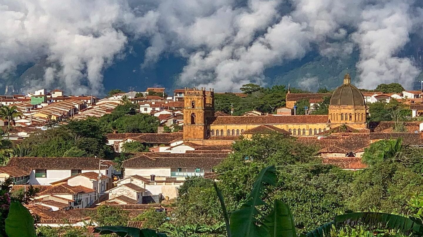 The morning clouds lift towards the mountains, and the morning sun lights warmly a Colombian town.